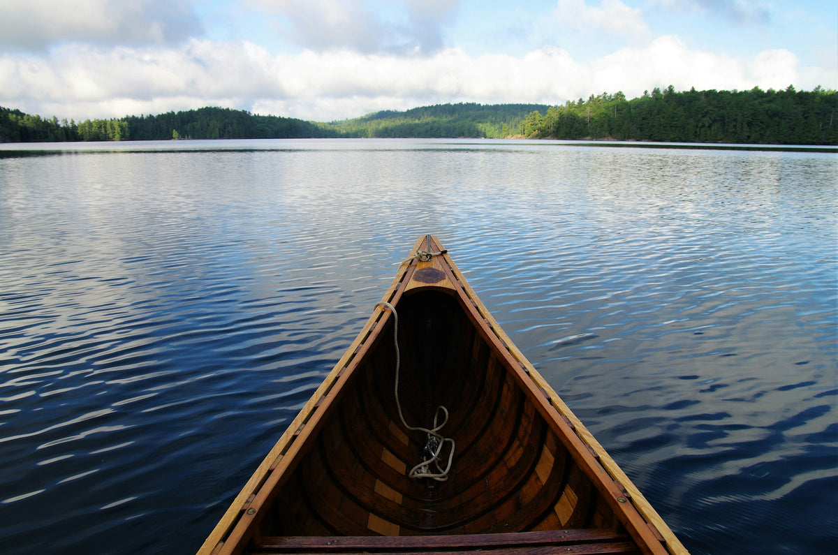 Looking past the bow of a wooden canoe across a calm lake